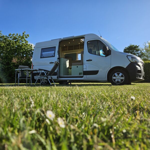 Camper auf einer grünen Wiese an einem sonnigen Sommertag.